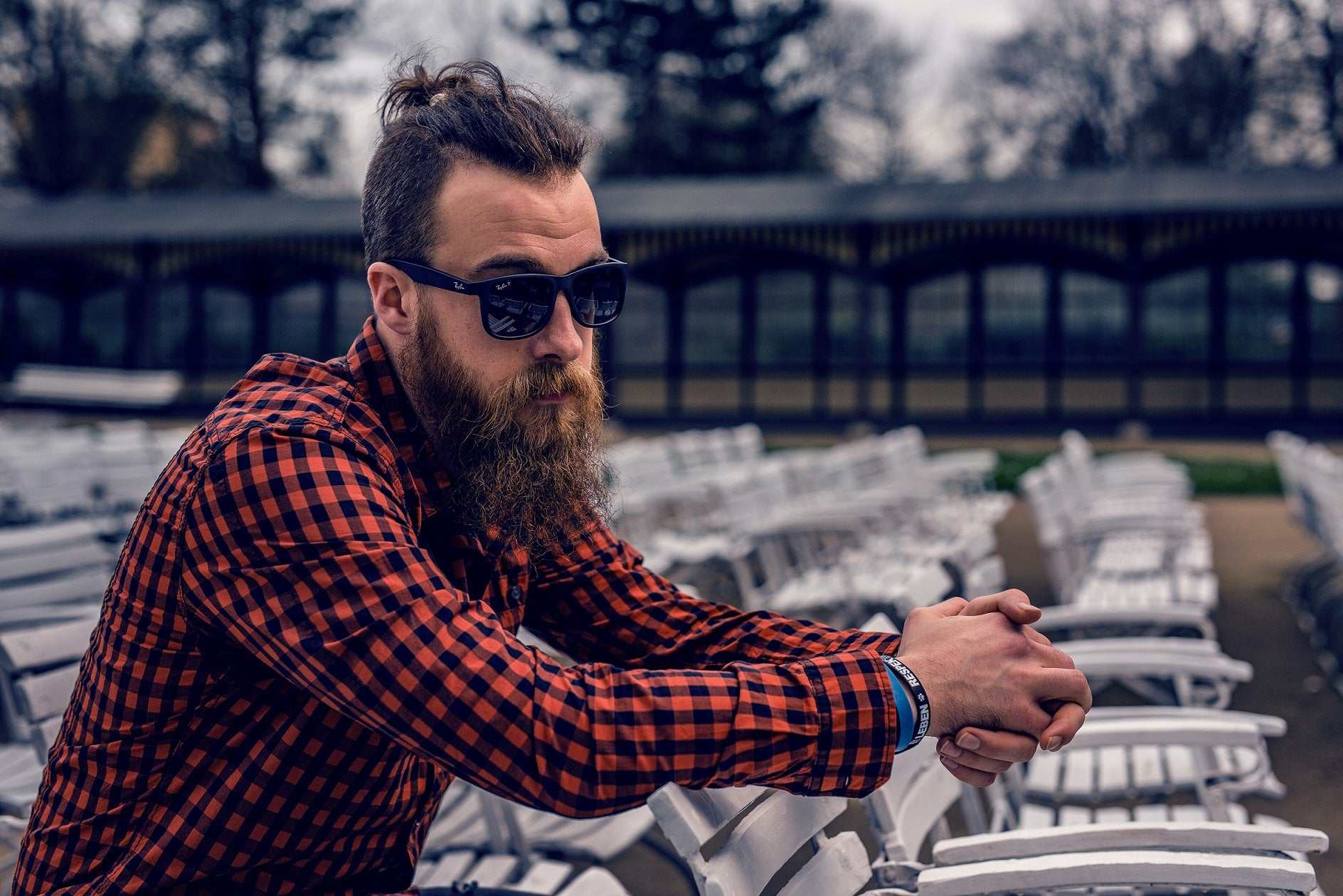 Man with thick beard and sunglasses wearing a red checkered shirt outdoors, representing deep nourishment with scented beard oil by Striking Viking