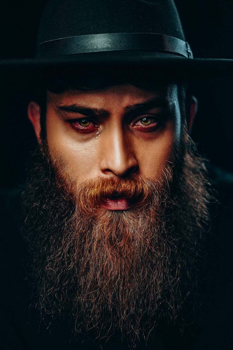 man with a long well-groomed beard wearing a black hat promoting beard grooming kit