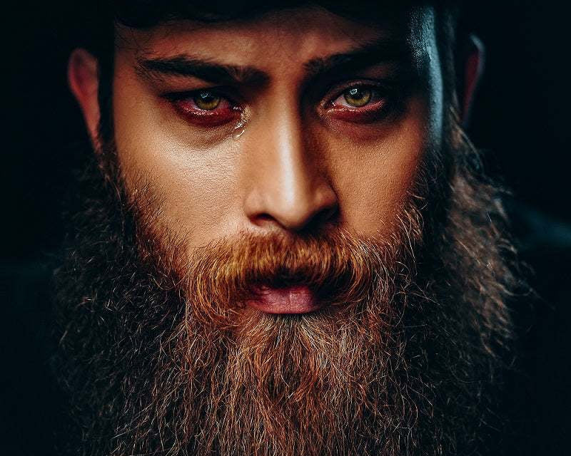 man with a long well-groomed beard wearing a black hat promoting beard grooming kit