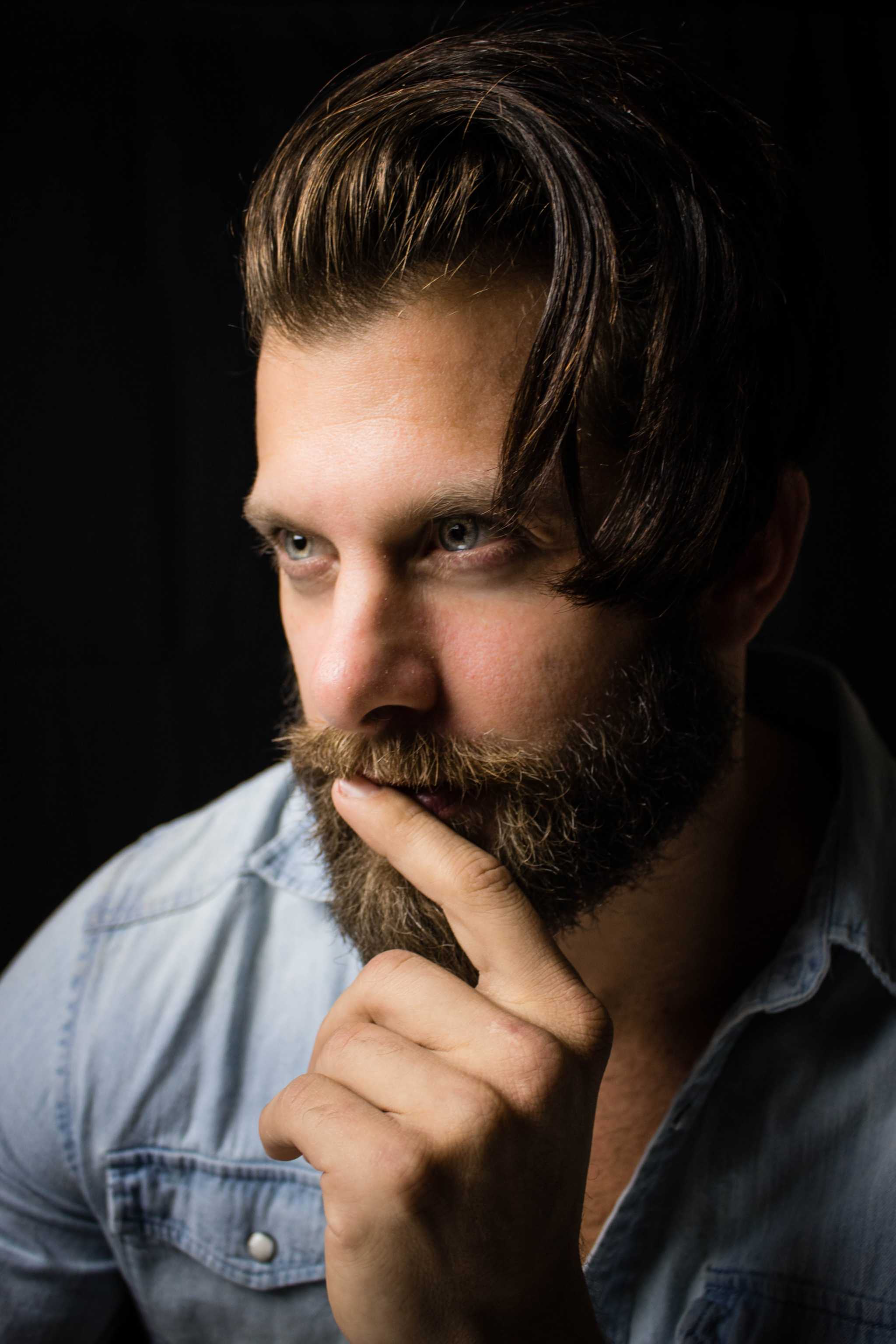 man with styled beard grooming his mustache thoughtful dark background Beard Grooming Kit