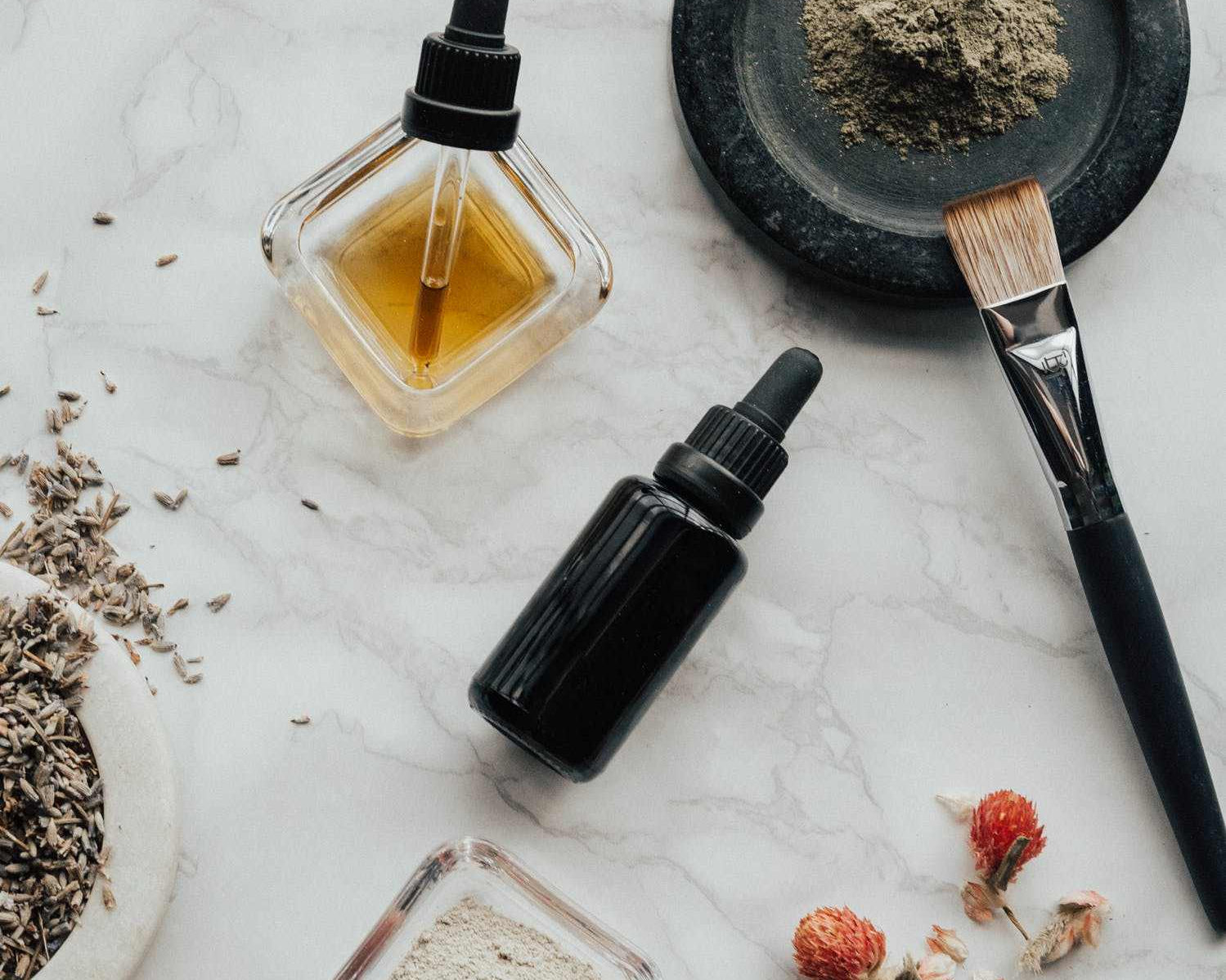 bottles of natural beard oil ingredients with dried flowers and powders on marble surface