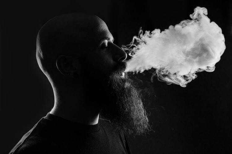 Bearded man exhaling smoke in profile with dramatic lighting highlighting Striking Viking beard grooming style